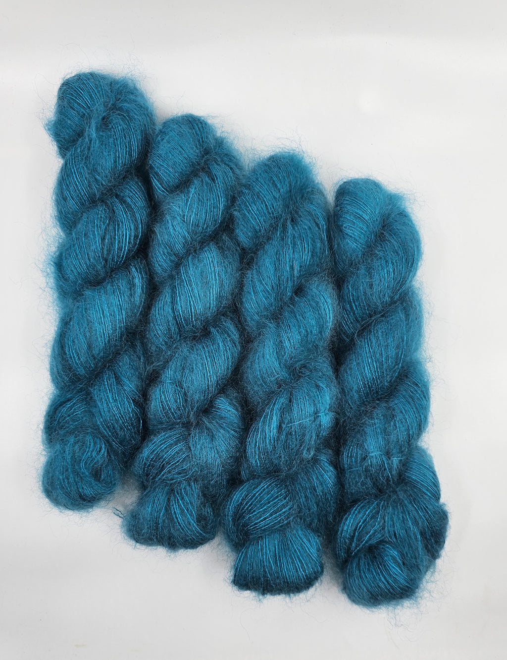 Three skeins of teal/blue mohair yarn on a white background