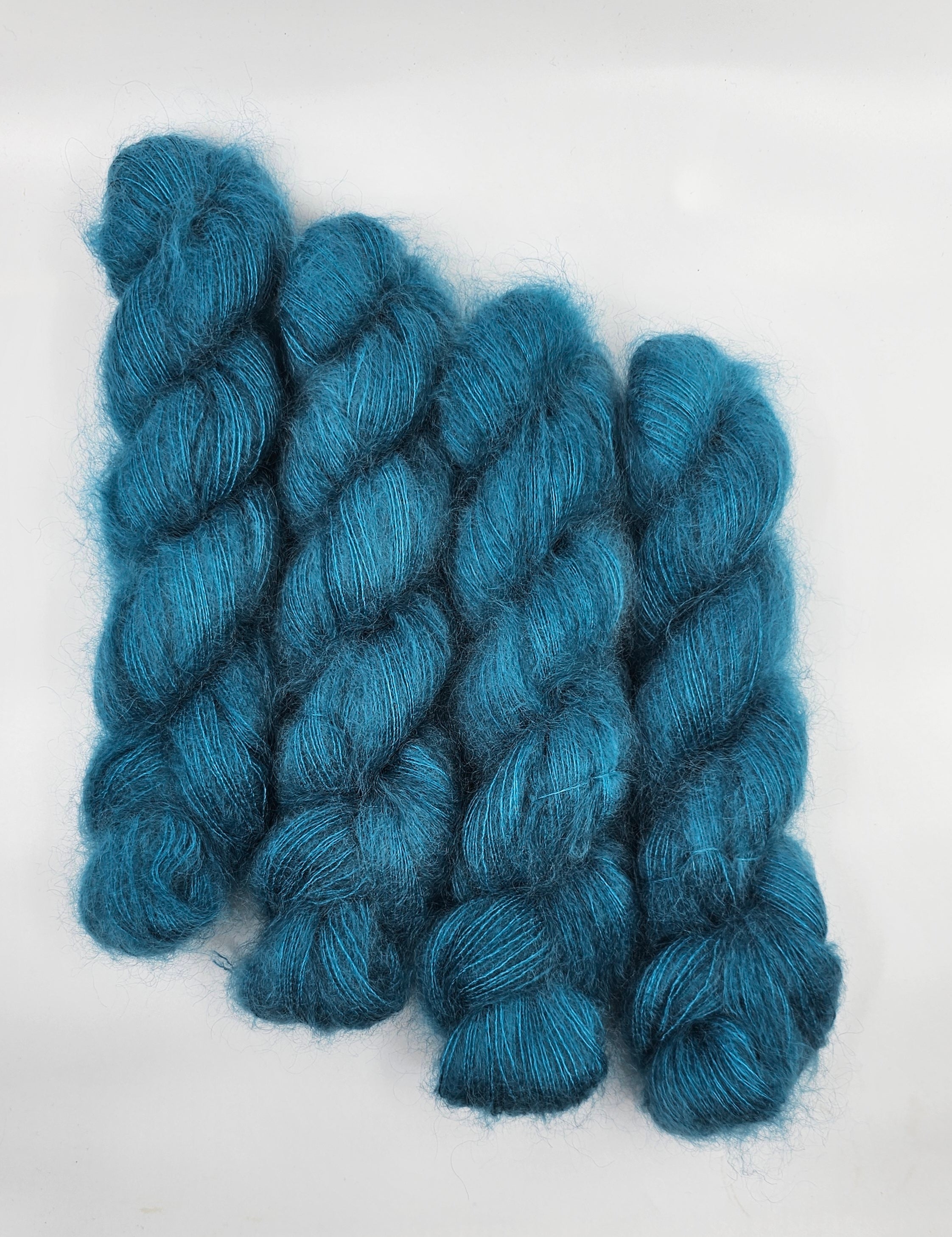 Three skeins of teal/blue mohair yarn on a white background