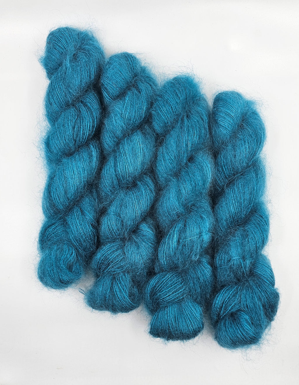 Three skeins of teal/blue mohair yarn on a white background